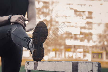 一个穿着黑色衣服的男人正在户外用障碍物锻炼运动场上的健身运动员有障碍的训练热身伸展双腿夏背景图片