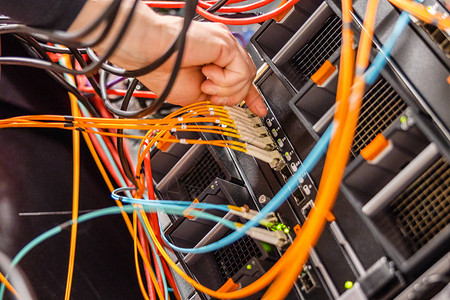 男信息技术工程师在刀片服务器网络开关中插入高速纤维电缆以便连接数据中心SA图片