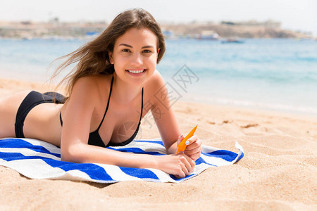 年轻女子躺在海滩的毛巾上在她的手上用图片