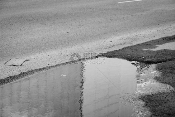 灰度道路上的水坑雨天倒映在水面上的建筑墙关闭俄罗斯冷漠悲伤的气氛沥青上的垃圾单色背图片