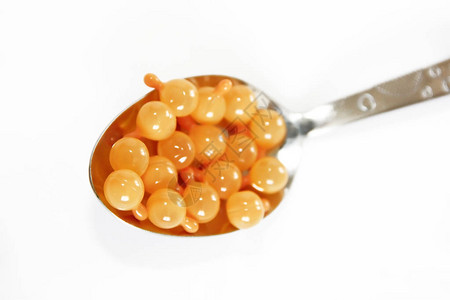 勺子白色背景中勺子里的橙色药胶囊背景