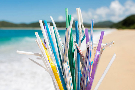 干净的海滩和海浪背景上的一堆用过的塑料吸管图片