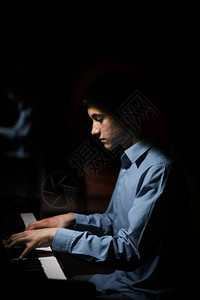 坐在钢琴前的年轻人男孩情绪激动地在音乐学校弹奏键盘乐器学生会玩手钢琴家黑色深图片