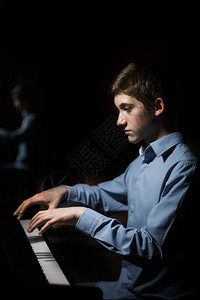 坐在钢琴前的年轻人男孩情绪激动地在音乐学校弹奏键盘乐器学生会玩手钢琴家黑色深背景图片