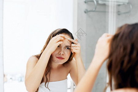 年轻女子看着和挤脸上的粉刺皮肤护理皮肤女孩的问题图片