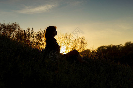 一位年轻浪漫女坐在日落时的山丘上图片