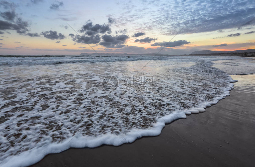 带有泡沫的大浪在海岸的沙滩上蔓延令人难以置信的日落之光反射在海面上黎明前的时间美丽的启蒙天空与云彩山脉浪图片