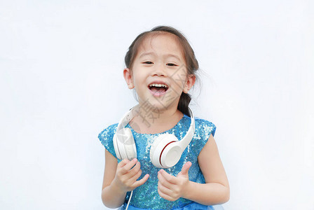 可爱的亚洲小女孩穿着漂亮的衣服听音乐用耳机在白色背景图片