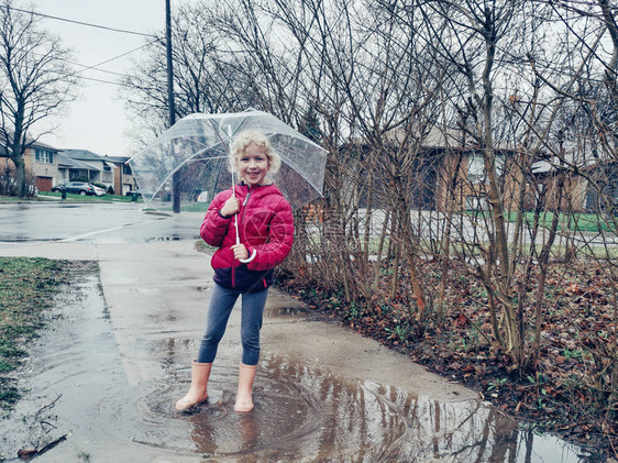 学龄前白人小女孩在外面的春秋日雨中跳进水坑里溅起水花有透明白伞的活跃儿童孩子享受生活快乐的图片