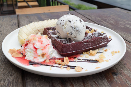 巧克力华夫饼配香草冰淇淋香蕉生奶油和草莓糖浆舒适的户外咖啡馆里的图片