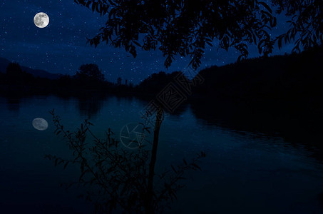 月亮在深蓝色的夜空中飞涨云彩和美丽平静的湖泊反射都背景图片