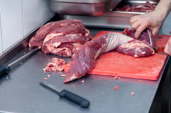 男子屠夫厨师在红色塑料板上用刀切下里脊肉片生牛肉和猪肉的特写手农贸市场烧烤用图片