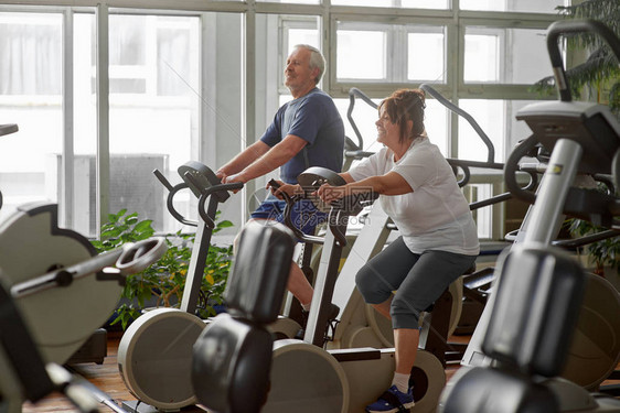 在健身房骑自行车的老年人老夫妇在健身中心做室内自行车健图片