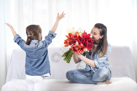 母亲节快乐带着一大束郁金香的可爱小女儿祝贺她的母亲在客厅的内部图片