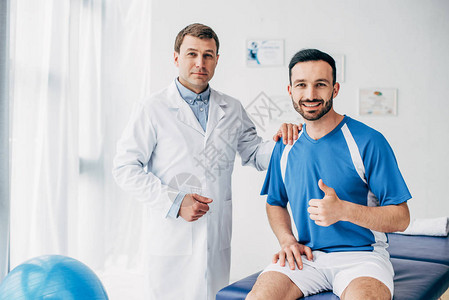 带着微笑的生理治疗师在足球运动员面前露出大图片