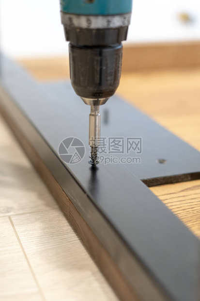 木匠使用专业电动螺丝刀仪器和修理固定在建造新的木桌或带金属腿的桌面上的垂图片