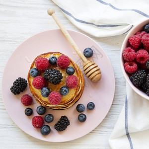 堆满煎饼夹着浆果和蜂蜜在粉红色的盘图片
