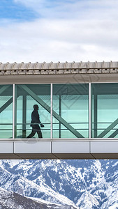 一个人在连接建筑物的天桥内行走的清晰垂直轮廓人行道可以看到冬天多云的天空映衬下一座引人注目的白图片