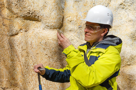 戴头盔和防护眼镜的雄地质学家检查了岩石对矿床图片