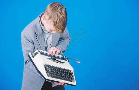 使用打字机小孩在旧打字机上打字有老式打字机的聪明的男生有打字机的可爱男孩小男孩拿着蓝色背景的复古打字图片