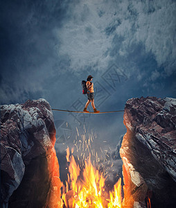 克服超现实的挑战女人在两座山峰之间有火焰的缝隙上方的松弛绳索上克服障碍承担风图片