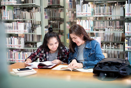 两名亚洲女学生在公共图书馆打开阅读杂志和微笑放松在国际学院大学的图片
