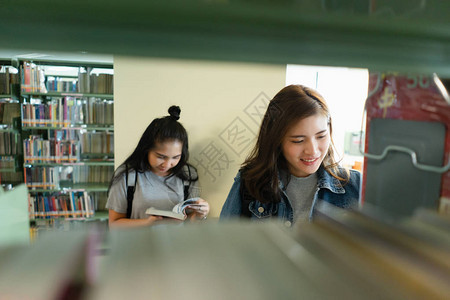 亚洲学生在国际学院大学图书馆的书架上寻找课本为准备大学考试的问题图片