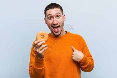年轻的caucasian男子拿着甜圈惊讶地对着自己指着自己图片