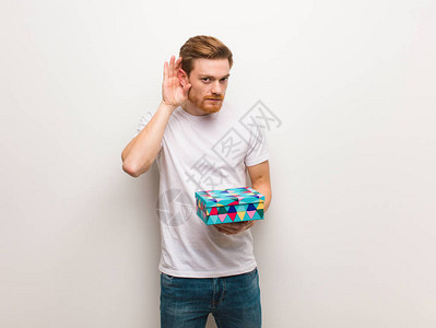 年轻的红发男人试着听八卦拿着一个礼盒图片