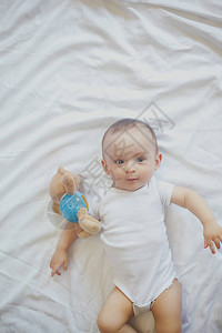 68个月大的男婴顽皮地躺在床上穿着白色紧身衣裤的迷人67个月小婴儿白色床上用品的男图片