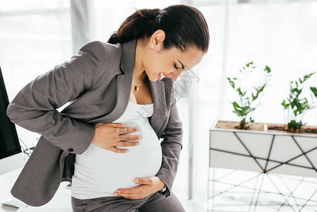 怀孕妇女因在任期间疼痛而抱着肚子并制图片