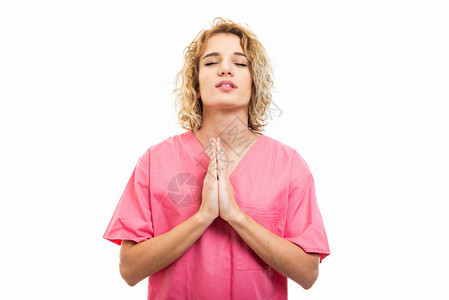 穿着粉色清洗剂的护士肖像将祷告手势孤立图片