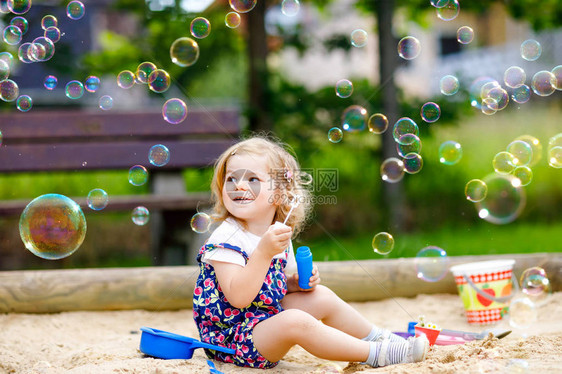 美丽的小金发蹒跚学步的女孩玩着吹肥皂泡鼓风机可爱的可爱宝贝孩子在阳光明媚的夏日在操场上玩耍快乐活跃有图片