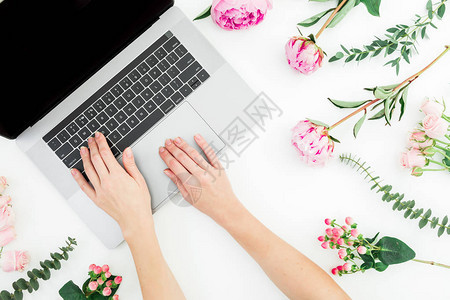 工作区与女手笔记本电脑和白色背景上的粉红色花朵图片