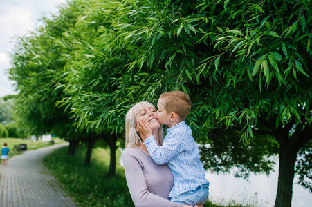 可爱的儿子亲吻妈在绿草和绿树的背景背景图片