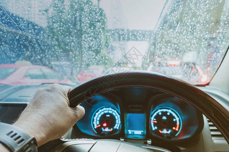 在雨天挡风玻璃上有雨滴的汽车方向盘上的司机的一只手危险图片