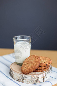 在木制桌上的条纹白餐巾上的圆棕全草面粉饼干和牛奶杯上图片