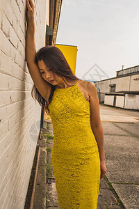 一个深思熟虑的亚洲中成年女穿着黄色蕾丝裙站在白砖墙对面看图片