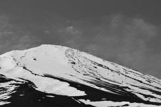 富士山的圆锥体在湛蓝的天空中升起一些薄雾从山的一侧吹过在前景中可以看到几棵树的顶部在一侧可以看图片