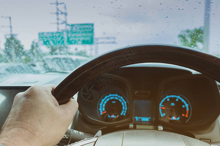 在雨天挡风玻璃上有雨滴的汽车方向盘上的司机的一只手危险图片