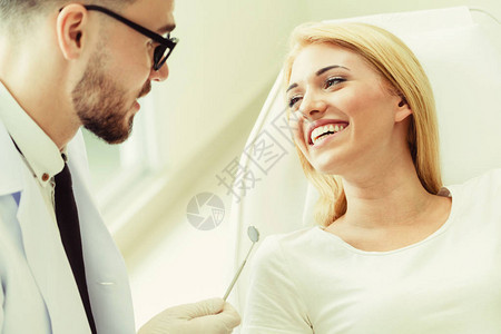 年轻英俊的牙医与坐在牙科诊所牙医椅上的快乐女病人交谈图片