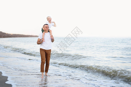 父亲肩上有个金发儿子正在海边走来图片