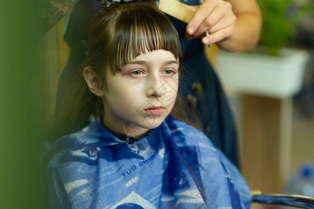 美发师给可爱的小女孩做发型女孩剪掉了刘海工作美发师更改图像改变发型时尚宝贝一系列理发婴图片