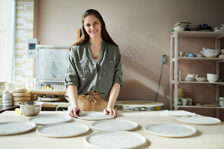微笑女工匠在陶艺车间布置手工陶瓷盘的肖图片