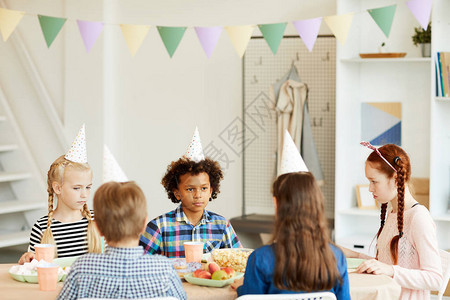 多族裔儿童庆祝生日的多民族群体儿童坐在咖啡厅的餐桌旁图片
