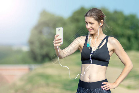 健身运动感女孩在锻炼休息期间在智能手机上制作自拍照片背景中的城背景图片