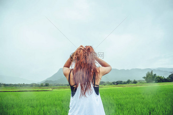 亚洲女旅行在假期放松站在雨中的草地上在雨季期间的图片