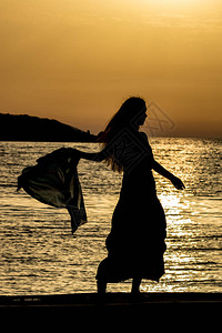 美丽的女剪影无法辨认的苗条高个女人与丝巾在的爱奥尼亚海水前夕阳从阿尔巴尼亚卡萨米尔看到的五颜六色图片
