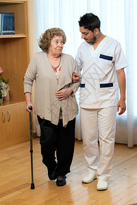 年轻男护士在客厅协助高龄妇女用拐杖助产的全长肖像背景图片