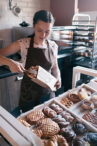 漂亮微笑的女工从小面包店的柜台陈列中挑选松饼卖给顾客图片